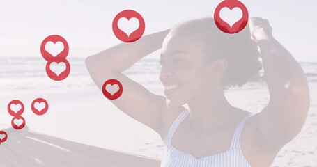 Standing woman in swimsuit holding surfboard fixing hair seaside with heart icons, copy space