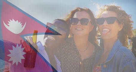 Smiling three friends wearing sunglasses standing on beach with calm water, holding beer bottle