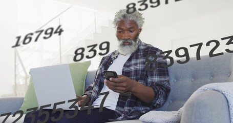 Typing on laptop, holding smartphone, man in plaid shirt surrounded by data overlays in living room