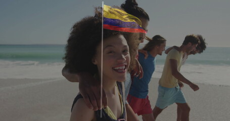 Walking group of five friends stepping through shallow water on sandy beach, with swimwear