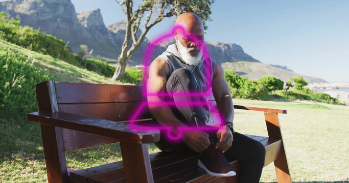 Tying shoelaces on running shoes African American man leaning on bench in grassy park, with earbuds