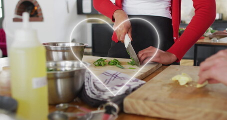 Chopping woman in red cardigan and partner slicing vegetables on boards in kitchen with steel bowls