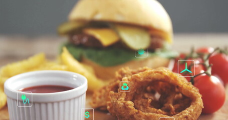 Displaying cheeseburger on dining table, beside French fries, onion rings, ketchup, cherry tomatoes