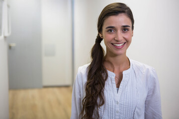 Woman in twenties standing in lit corridor wearing button-up blouse by frosted door, copy space