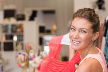 Woman holding coral pink dress on hanger in boutique store among racks and accessories, copy space