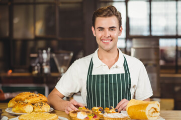 Male baker wearing green-striped apron arranging pastries on wooden counter in bakery kitchen