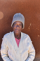 Africa village, single old african woman sited on a chair in front of the thatched roof mud house