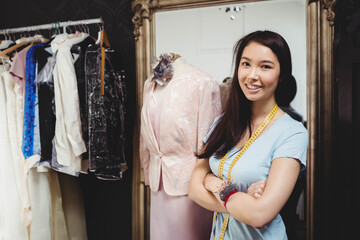 Asian woman posing inside tailoring boutique next to mannequin with measuring tape and pin cushion