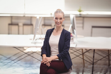 Businesswoman sitting on swivel chair in modern office working at dual monitors wearing navy blazer