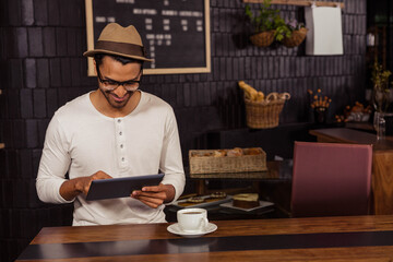 Tablet is resting on wooden counter, with white coffee cup sitting on saucer near wicker baskets