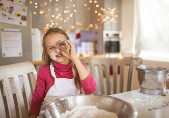 Child girl holding cookie cutter over eye mixing flour in bowl on table at home kitchen