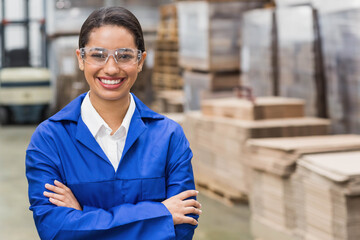 African American woman wearing coverall and goggles standing in warehouse with pallets and forklift