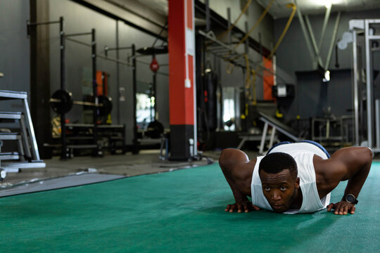 Muscular man is performing push-ups on green turf at fitness facility near weight plates