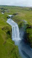 Obraz premium Skogafoss waterfall, surrounded by vibrant green landscapes, tumbles gracefully into a serene river below in Iceland