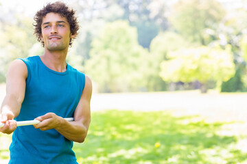 Man pulling thick white rope in sunlit park wearing turquoise sportswear on green grass, copy space