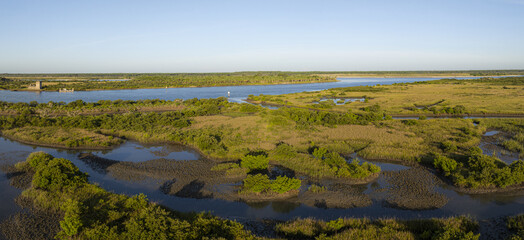 Aerial view of winding waterways reflecting the clear sky, cutting through the lush green and golden marshlands under the soft light around Fort Matanzas, St. Augustine, Florida, United States.