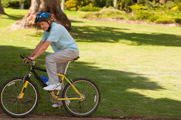 Senior man riding yellow bicycle with blue helmet, water bottle on frame in park, copy space