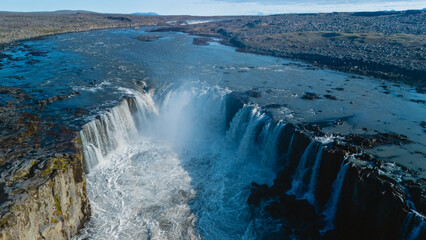 Selfoss waterfall pours dramatically into the river below, surrounded by rugged terrain and unique geological formations in Iceland. The stunning view captures the essence of natures raw beauty.
