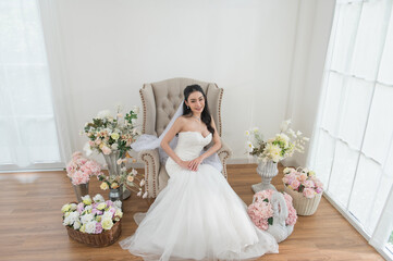 Wedding, Bride in beautiful dress sitting on sofa indoors in white studio interior, Young...