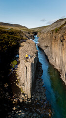 Two adventurers stand atop towering basalt columns at Studlagil Canyon, surrounded by pristine...