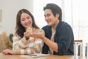 Happy Asian family young couple in love hand holding model house and showing keys for saving money...