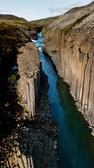Discover the dramatic beauty of Studlagil Canyon, where turquoise waters flow between towering...
