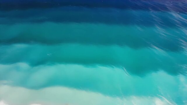 An abstract aerial or side-view of a large, powerful ocean wave, showing a beautiful gradient of deep blue and turquoise water