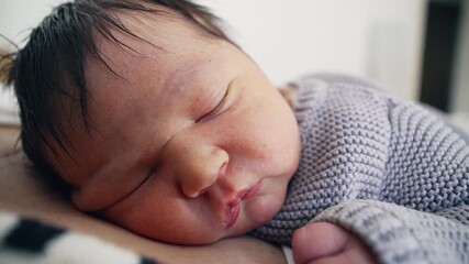 Tight macro close-up of newborn baby infant in deep sleep resting on mother's chest during first week of life