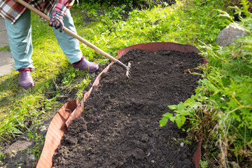 An older woman with blonde hair works in the garden. A woman is digging garden beds.