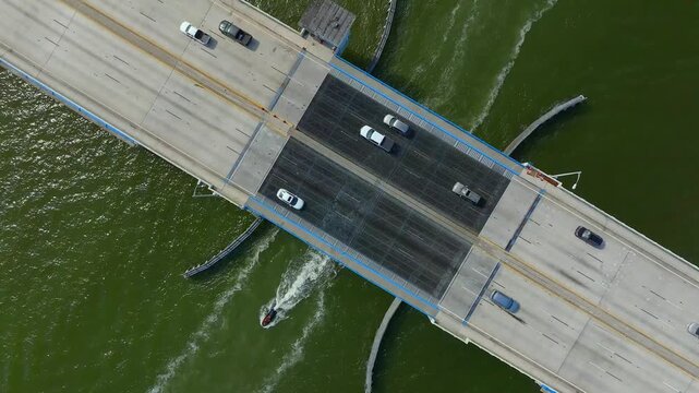 Aerial view of the 79th Street Causeway, with vehicles traversing the bridge and a boat speeding below, contrasting with the dark water, North Bay Village, Florida, United States.