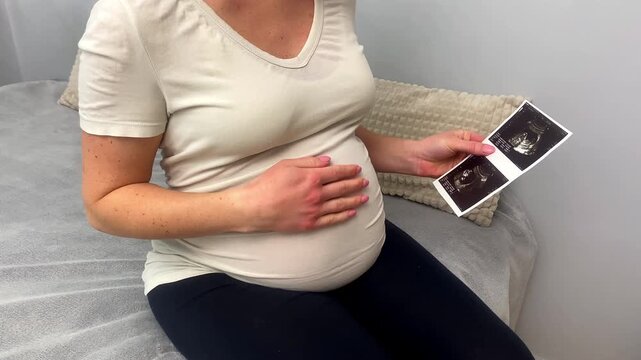 Expecting pregnant woman on bed looking at ultrasound scans photo of fetus.Future mom waiting child baby,boy or girl,pregnancy,birth and motherhood concept.