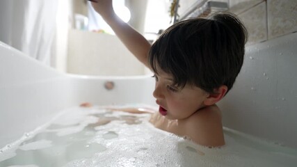 Young boy in bathtub, close-up, blowing bubbles, indoor setting, natural light, curious expression, casual and fun moment, simple background, childhood and joy - Powered by Adobe