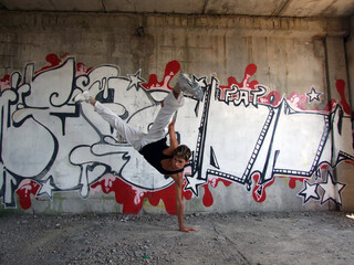 A guy does a back somersault with an arched back while jumping from a large black tire standing in...