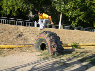 a guy in a yellow t-shirt doing a parkour style trick through a large tractor tire at the stadium...