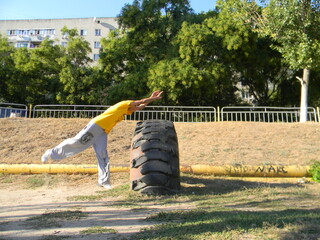 A guy makes an acrobatic stunt fly roll in parkour style through a large tractor tire in the...