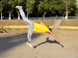 A guy does an acrobatic trick in parkour style against the backdrop of trees and city houses at the stadium	
