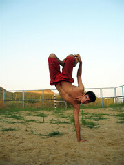 A guy performs an acrobatic stunt standing on one hand on the sea against the backdrop of a gate	
