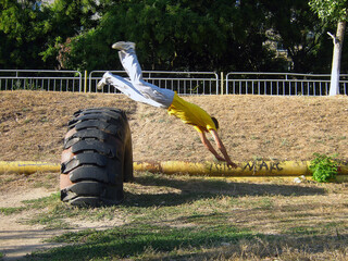 A guy performs an acrobatic fly roll stunt through a huge tractor tire landing on the grass	
