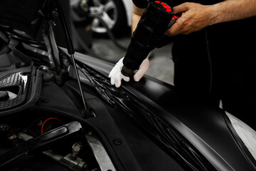 Car Vinyl Wrapping with Heat Gun. Applying black vinyl wrap to car with heat gun ensures precise adhesion and flawless surface coverage. Heat gun used in vinyl wrapping activates adhesive.