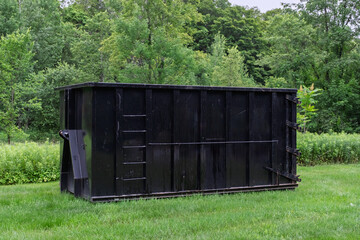Large 30 Yard Black Roll-Off Dumpster in a Grassy Yard with Trees in Background