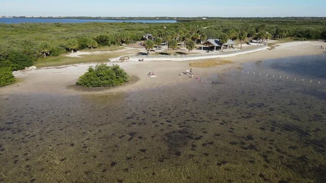 Drone orbits to the right low over shallow waters and marked swimming area at the beach in Robert K Rees Memorial Park in Florida, USA