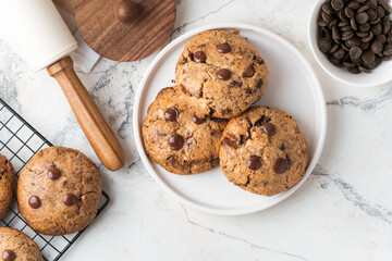 Fresh chocolate American chip cookies with nuts and chocolate drops on white marble background. Flat lay of cookies with stylish cutlery and pastry chef accessories. Recipe of homemade cookies concept