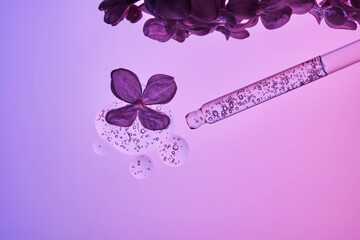 Cosmetic pipette with serum and lilac flowers on a purple background.