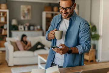Freelancer enjoying morning coffee and checking smartphone at home