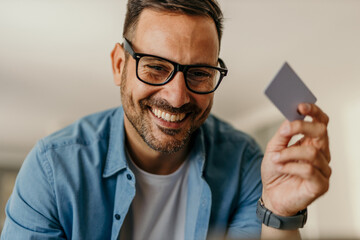 Happy man holding credit card, enjoying online shopping perks at home