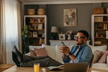 Entrepreneur relaxing with feet up on desk using smartphone at home