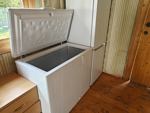 White chest freezer with open lid in a rustic kitchen setting showcasing wooden flooring