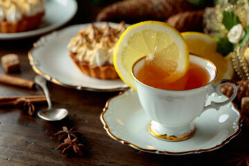 White cup of tea with lemon and meringue tartlet.