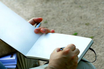 Hand of a young man writing or holding a blank notebook, sitting on a bench.