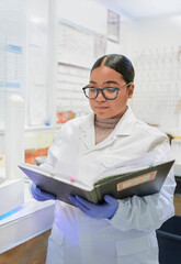 Young latina woman researcher stands in a science lab with a research notebook, wearing a lab coat...